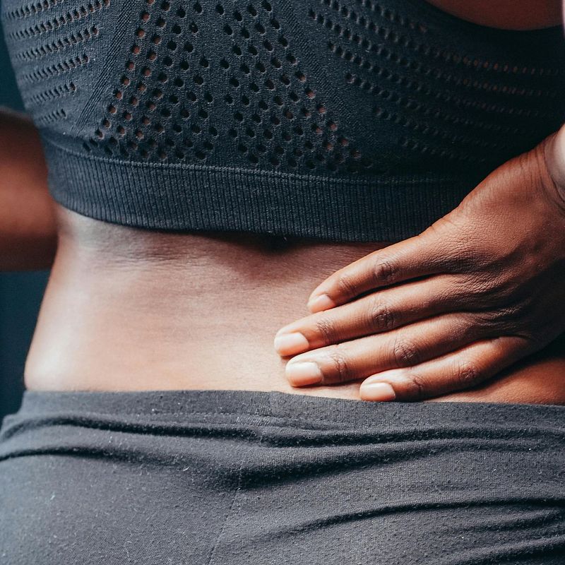 woman wearing exercise clothing holding her back in pain