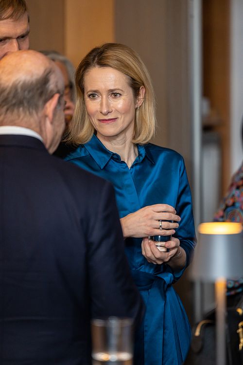 Kaja Kallas holding a glass in her hand, engaged in conversation with a middle-aged man.