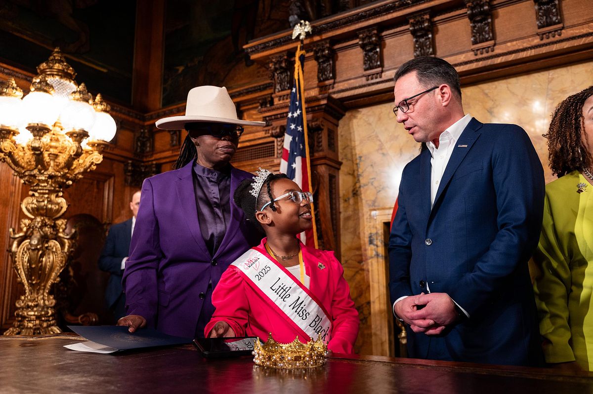Governor Josh Shapiro speaks with a young girl wearing a &ldquo;Little Miss Black&rdquo; sash during the CROWN Act signing ceremony in Pennsylvania, capturing a meaningful moment of leadership, representation, and community impact.