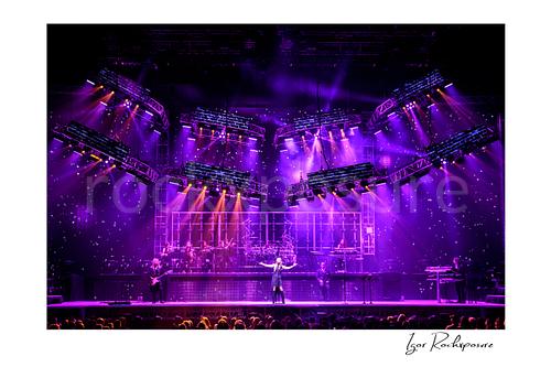 Horizontal color image of Trans Siberian Orchestra performing on stage beneath purple lighting with the full band and orchestra visible