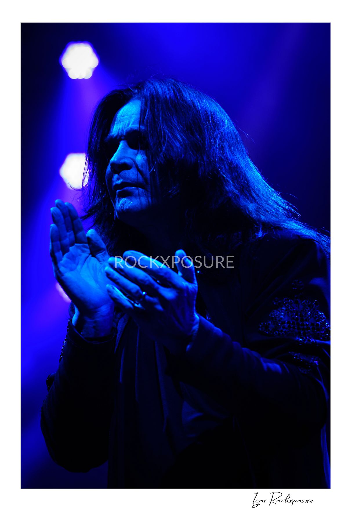 Ozzy Osbourne of Black Sabbath illuminated by deep blue stage lighting holding a microphone during a live performance